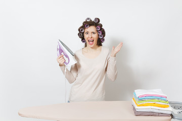Crazy fun housewife with curlers on hair in light clothes ironing family clothing on ironing board...