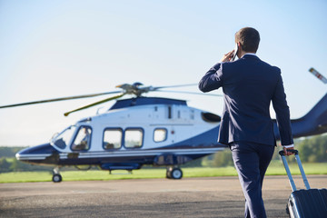 Rear View Of Businessman Walking Towards Helicopter Whilst Talking On Mobile Phone