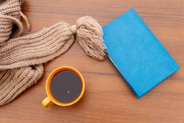 Cup of coffee, knitted scarf and book on wooden background