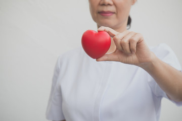 Senior female nurse holding red heart symbol in her hand; isolate on white