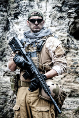 Fototapeta premium Prywatny wykonawca wojskowy PMC w czapce baseballowej z karabinem szturmowym w skałach