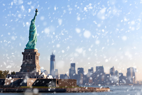 The Statue of Liberty free of tourists and New York City Downtown on sunny early morning during snowfall.