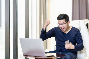 Young happy excited asian man watching laptop and celebration, winning, satisfaction, cheerful action with success work.
