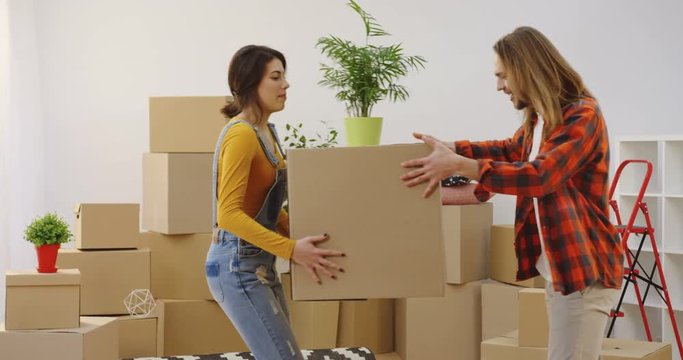 Young happy lovely couple bringing a plant and box in the living room while moving in together. Inside