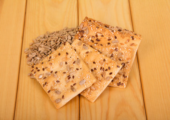 The biscuit is sprinkled with sesame seeds, sunflower seeds are scattered near it, against background of wooden surface