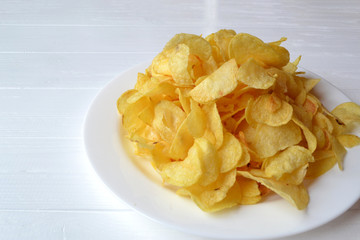 Chips in the white plate on the white wooden table. Fast food. Fried potatoes.