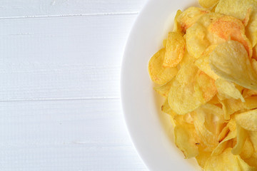 Chips in the white plate on the white wooden table. Fast food. Fried potatoes.