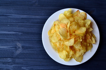 Chips in the white plate on the blue wooden table. Fast food. Fried potatoes.