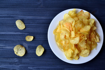 Chips in the white plate on the blue wooden table. Fast food. Fried potatoes.
