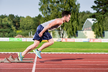 Athlete on cinder track of sports facility at the moment he starts to sprint