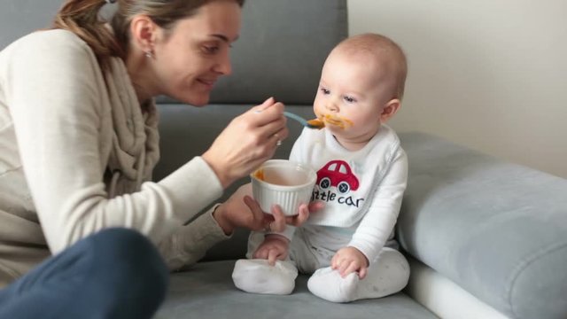 Mother, feeding her baby boy with mashed pumpking for the first time