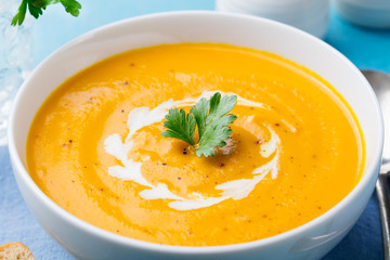 Pumpkin and carrot soup with cream and parsley on blue stone background. Close up