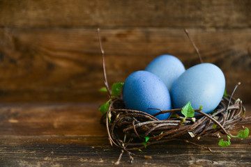 Easter decor, background: painted eggs of blue color in a decorative nest with branches of greenery, the concept of the spring festival, the arrival of spring. The layout for your text.