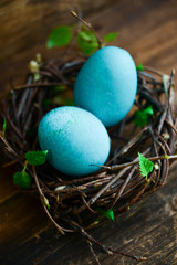 Obraz na płótnie Canvas Easter decor, background: painted eggs of blue color in a decorative nest with branches of greenery, the concept of the spring festival, the arrival of spring. The layout for your text.