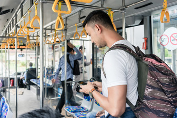Young male tourist with a big backpack using the mobile phone for guidance or communication while standing in the bus in Jakarta