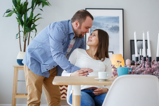 Image of happy husband hugging pregnant wife sitting at table with candles