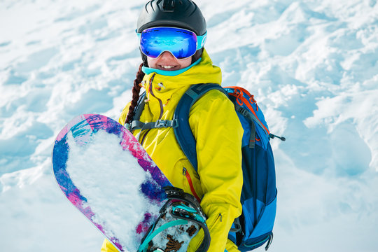 Photo of smiling woman in helmet and with snowboard in background of snowy landscape