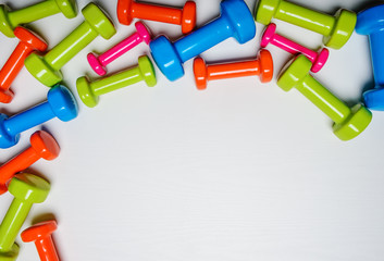 many blue green and one orange in the middle dumbbells on a white background ,concept preparing to fitness sports equipment top view mock up