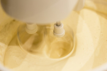 A kitchen mixer with yellow egg yolks mixed with sugar in a modern kitchen. Shot at an angle with the mixer whisk clearly visible