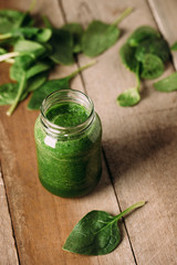 Green spinach juice jar on a rustic wooden table and spoon