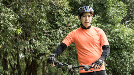 Young asian man in orange sportswear and mountain bike during recreation time in the park, Beautiful sunny day.