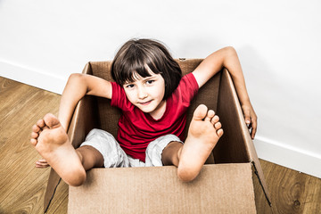 relaxed child sitting in old cardboard box with feet out