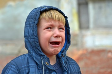 A boy in a blue jacket in a hood, crying with tears