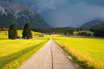 Sunlit country road in Alps, rain straight ahead