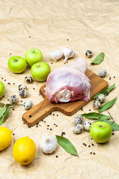 Raw turkey thigh garlic apples lemon quail eggs spices on a wooden board. Top view of a turkey, knife on a beige paper background. Culinary background, ingredients for cooking.