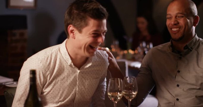 4K Attractive smart-casual men chatting & laughing over a glass of wine in restaurant, could be friends or business colleagues.. Slow motion