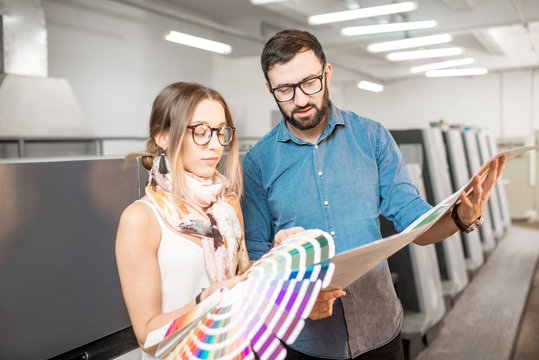 Young woman designer and print operator working together with color swatches standing at the print manufacturing