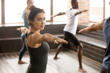 Jolie femme yogi et un groupe de jeunes sportifs pratiquant la leçon de yoga, debout dans l& 39 exercice Warrior deux, pose Virabhadrasana 2, entraînement, gros plan intérieur, studio