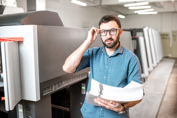 Portrait of a handsome typographer standing with stack of paper at the printing manufacturing with...