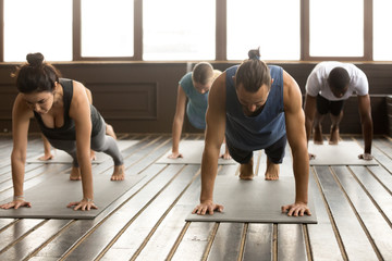 Group of young yogi people practicing yoga lesson standing in Plank pose, doing Push ups or press...