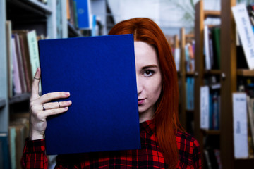 Beautiful redhead girl with blue book in a library