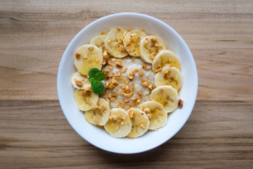 Oatmeal with banana, dried nuts and honey in white bowl on wood table closeup. Natural health dieting food