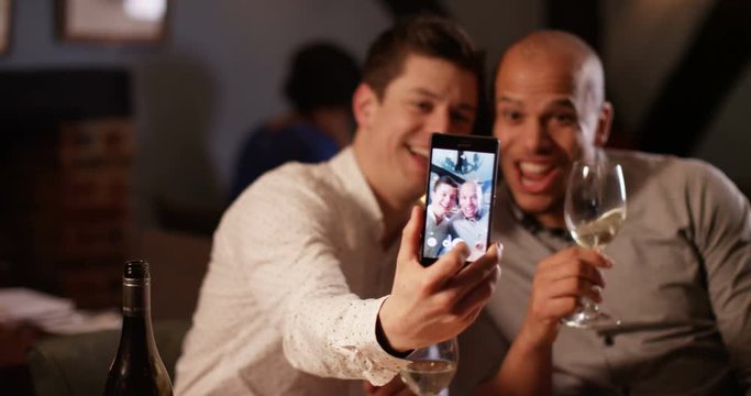 4K Happy male friends enjoying glass of wine on an evening out pose to take a selfie with smartphone