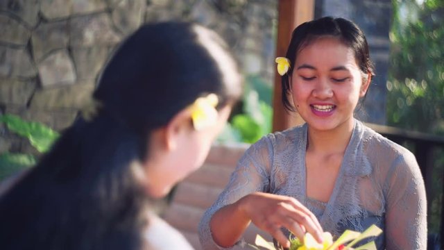 Two young balinese women chatting while making canang sari offerings in Ubud, Bali