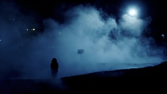 Silhouette of woman walking through the mist  at night. Illuminated by night.