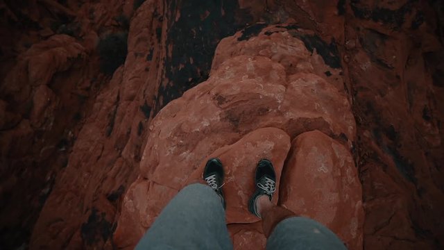Looking Down at Feet Walking on Narrow Rocky Cliff above Canyon