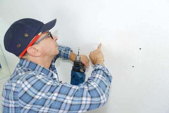 seniro man drilling a hole in a wall