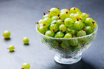 Gooseberries in glass bowl on black stone slate background. Copy space.