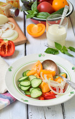 Vegetarian healthy salad with fresh ripe summer vegetables: tomato, cucumber, pepper and onion on light wooden background.