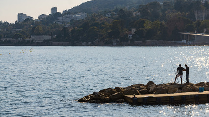 Two men fishing at stone coast in Vallauris, Cote d'Azur