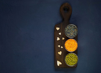 Concept of vegetarian food. Cereals and legumes in metal cups on a wooden texture with hearts on a blue background of concrete. Top view, empty space for text