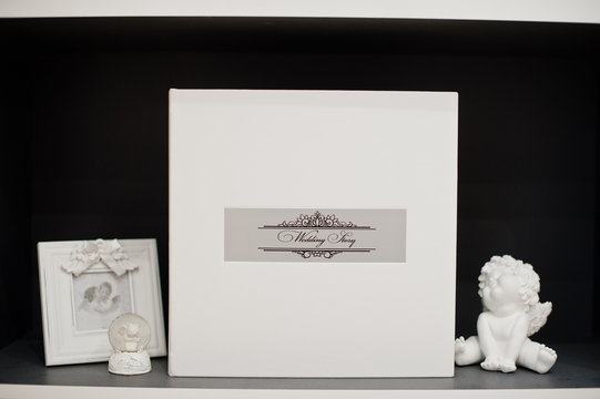 Elegant white or beige photobook or photo album on the self next to the small cupid statue and frame.