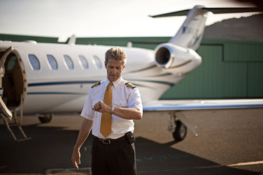 A pilot looking at his watch while standing in front of a private jet