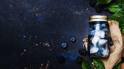 Summer berry drink in bottle with blueberries, blackberries and ice, top view