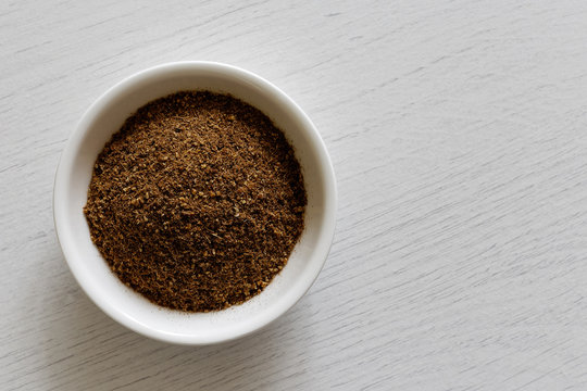 Ground cumin in white ceramic bowl isolated on white wood background from above.