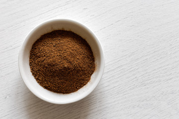Ground cloves in white ceramic bowl isolated on white wood background from above.